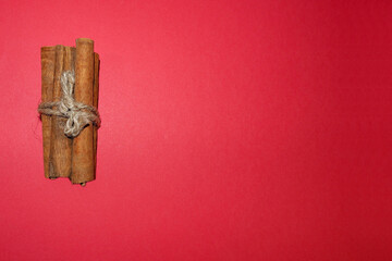 a few brown sticks of cinnamon tied with a thread on a red background at the top . Christmas symbols and baking spice