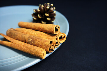 brown cinnamon sticks and a cone with gold acrylic paint as a Christmas decoration on a gray plate on a black background side view . Christmas symbols