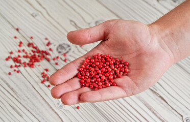 Red or Pink peppercorn in young man hand, more scattered on white boards desk below, closeup photo