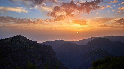 Postcard from Madeira. Sunset over mountains from the highest point of mountain Pico do Arieiro. Twilight, sun touches ocean. Tranquil moment. Traveling around Madeira Island, Portugal.