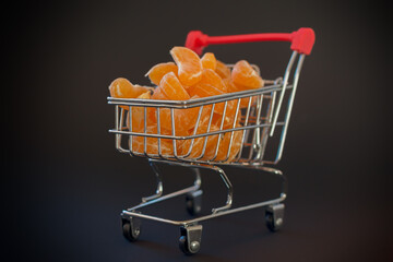 Fresh, juicy, peeled mandarin slices in a shopping trolley on a black background. Concept - in the...