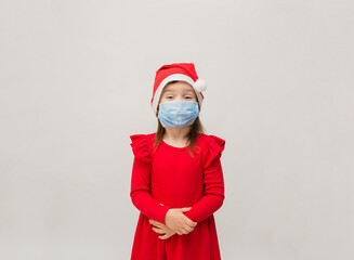 little girl in a red dress and a new year's cap in a medical mask on a white background with space for text