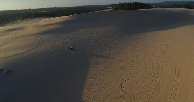 Wide aerial, atv drives on sand dunes in Oregon