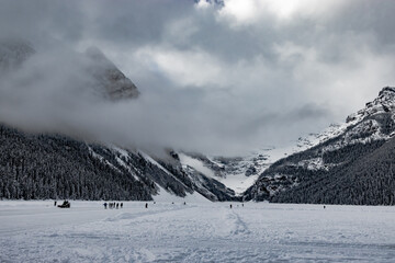 Beehive and Devils Thunb watch over ice skaters with clouds rolling by. Lake Louise. Banff National Park, Alberta, Canada