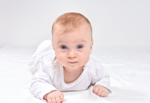 Adorable caucasian baby 3(three) months, blue-eyed, blond, lying on stomack on a white blanket, looking at camera. Newborn concept.