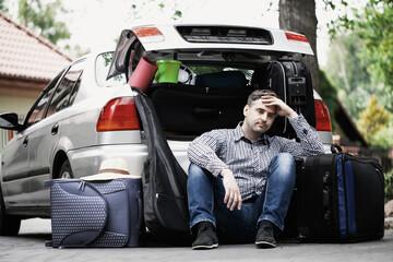 Handsome man sitting on the road next to car with open trunk