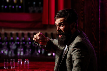 Vintage worker man with long beard holding whiskey. Sitting in bar.