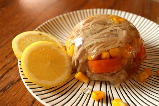Poultry jelly (galantine) with corn and carrots, served with lemon slices on a black and white plate