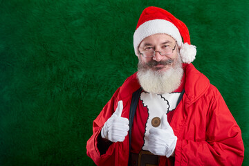 Mature bearded man with eyeglasses on face wearing Santa hat, Santa shows two thumbs up, copy space