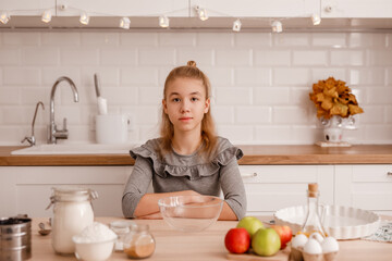 Blonde teenage girl in a gray dress is going to cook traditional apple pie in the new kitchen