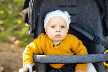 A little girl 1 year old dressed in a yellow shirt and a white hat sits in a grey stroller in the...