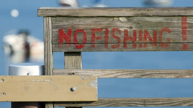 Close video of no fishing painted on a wood railing with the ocean in the background.