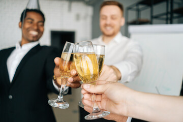 Close-up view of business team of multinational employees holding clinking glasses of champagne and smiling cheerfully at corporate New Year or Happy Christmas eve.