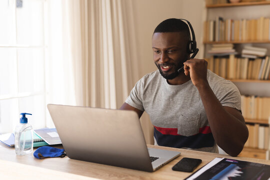 African american man using phone headset while having a video chat on laptop while working from home