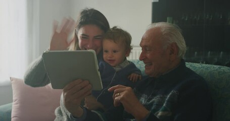 Cinematic shot of happy family: grandfather, daughter and grandson baby having fun to make selfie or video technology call to family and relatives with tablet or smartphone on sofa in living room at h - Powered by Adobe
