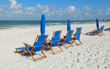 Blue beach chairs and umbrellas facing the Gulf of Mexico on a beautiful day in Fort Myers Beach, Florida, USA.