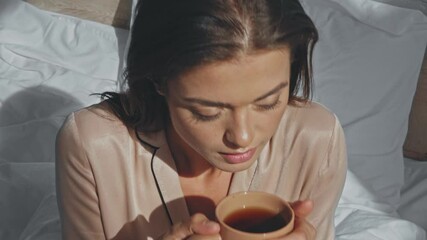 joyful woman drinking tea while sitting in bed - Powered by Adobe