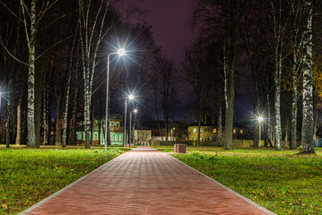 Park landscape with a bench, footpath and night lighting.