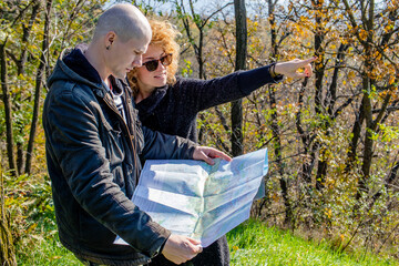 Fototapeta premium Happy young couple reading a map, looking for a route or location for a hiking at country in autumn. Travel, trip, searching leisure and lifestyle concept. 