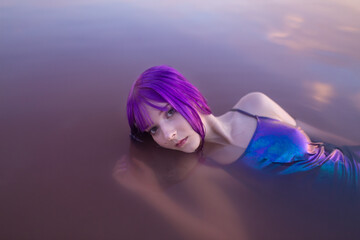 Young gorgeous girl with pale skin, dyed purple hair in a pink lake, concept of youth and beauty...