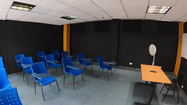 Aula escolar toma abierta con sillas azules, pupitres y fondo negro