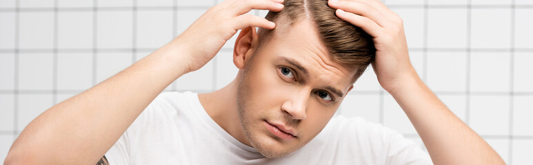 Worried young adult man checking hair in bathroom, banner