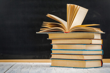 A stack of books on a white table against a blackboard.