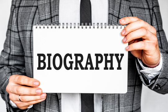 business, technology, internet and networking concept - businessman in gray fashionable business suit holding a white notebook with conference inscription BIOGRAPHY inscription