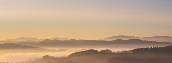 misty landscape at sunset, mountains rising from clouds of fog in the background, clear sky