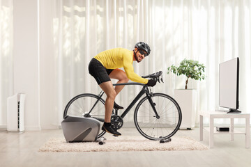 Full length shot of a young man cycling with a trainer bicycle at home