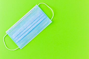 Face protective mask on a green background. Medical mask for protection against coronavirus. Healthcare and medical concept. Copy space. Top view