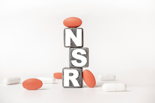 a group of white and red pills and cubes with the word NSR Normal sinus rhythm of the heart on them, white background. Concept carehealth, treatment, therapy.