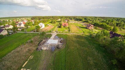 Aerial view on detached house under construction. House In foundation state. Located on green plot in small village. Wooden roof structure. Meadows around.