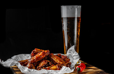 glass of fresh beer and fried chicken wings on wooden table on black background