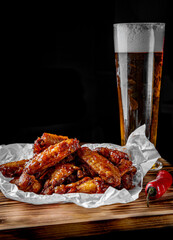 glass of fresh beer and fried chicken wings on wooden table on black background