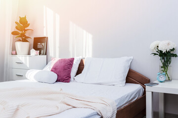 Lifestyle bedroom interior with pink and white pillows on bed in natural morning light.