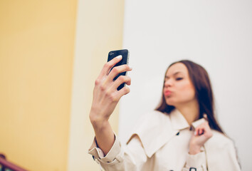 beautiful young girl in a light raincoat takes a selfie on her phone