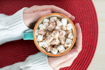 Cup of hot chocolate with marshmallows in woman's hands on the table
