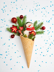 Snowman, fir twigs and Christmas toys in a waffle cone. White background with blue and white snowflakes. Christmas card. An original gift.