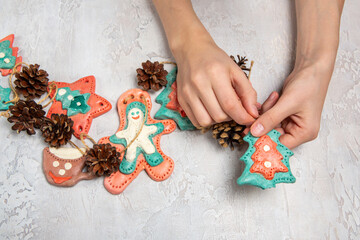 Homemade home decoration for Christmas. Children's hands are holding a homemade garland. Gingerbread men are made of salted dough, cones. Light background.