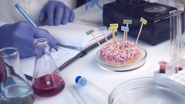 Food safety laboratory, scientist concept. Inspector doing research in lab. The donut on he table is decorated with tablets with the names of the additives of E.
