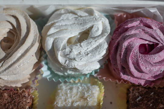 Sweet homemade dessert zephyr pink, beige, white - big marshmallows and 'bird milk' candies in a white gift box on a white table. handmade Big zephyr sprinkled with powdered sugar. Food photography