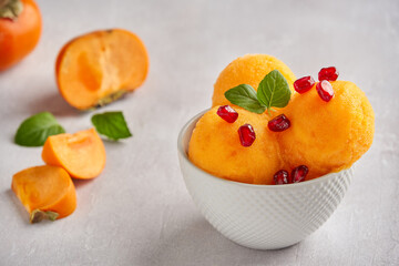 Persimmon ice cream , sorbet with pomegranate seeds and mint leaves. Closeup . 