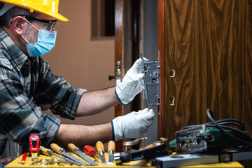 Carpenter worker at work repair and install a room door lock, wear the surgical mask to prevent...
