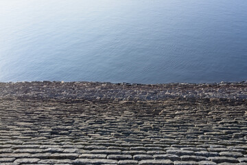 Half bright sunny blue water and half stone reservoir wall texture