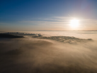 Fototapeta na wymiar Aerial view of sunrise above foggy town. Mystical fog scattering sunrays of upcoming sun.