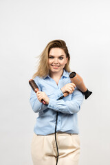 Photo of a woman on a light background. The girl is holding a hair hairdryer and a comb. She has a smile on her face. High quality photo.