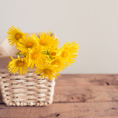 yellow flowers in a basket on a wooden background