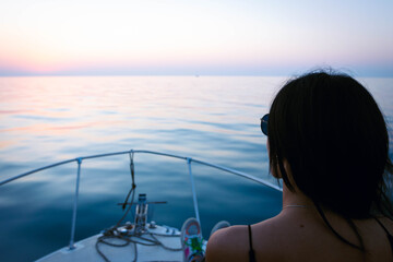 Woman sits in front of the boat and looks to blue black sea horizon after the sunset. Boat trips...