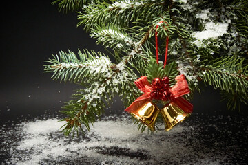 Christmas decoration with bells, a branch of a Christmas tree and artificial snow on a black background.